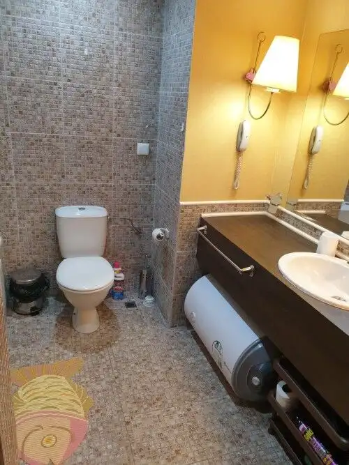 Bathroom with beige tiles, toilet, and vanity with sink in the apartment.