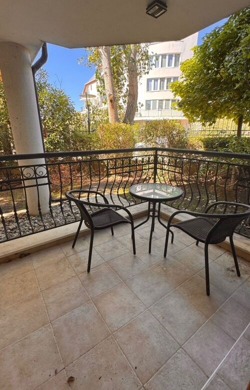 Outdoor balcony with black metal chairs and a small round table in a sunny residential area.