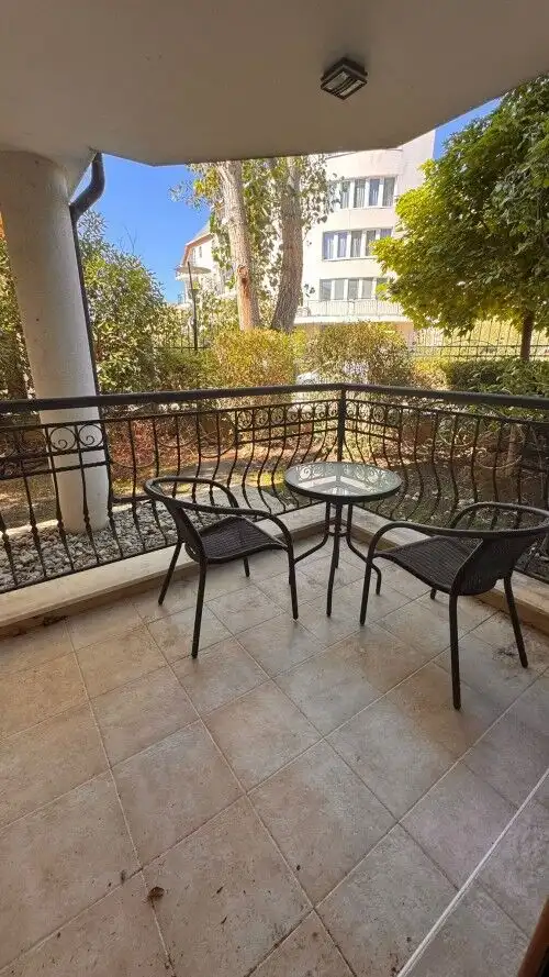 Outdoor balcony with black metal chairs and a small round table in a sunny residential area.