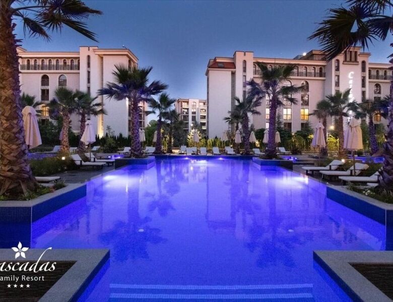 Pool view of Cascadas Family Resort with palm trees and elegant buildings at sunset.