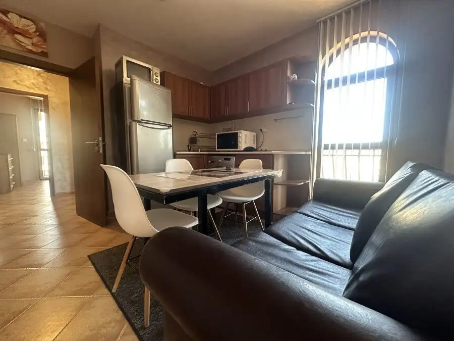 Interior of a 3-bedroom apartment with pool view, featuring a black leather sofa, dining area, and k.