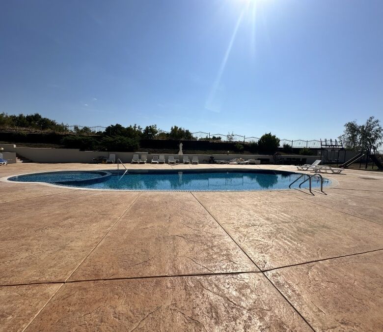 Outdoor swimming pool with sun loungers and bright sunlight.