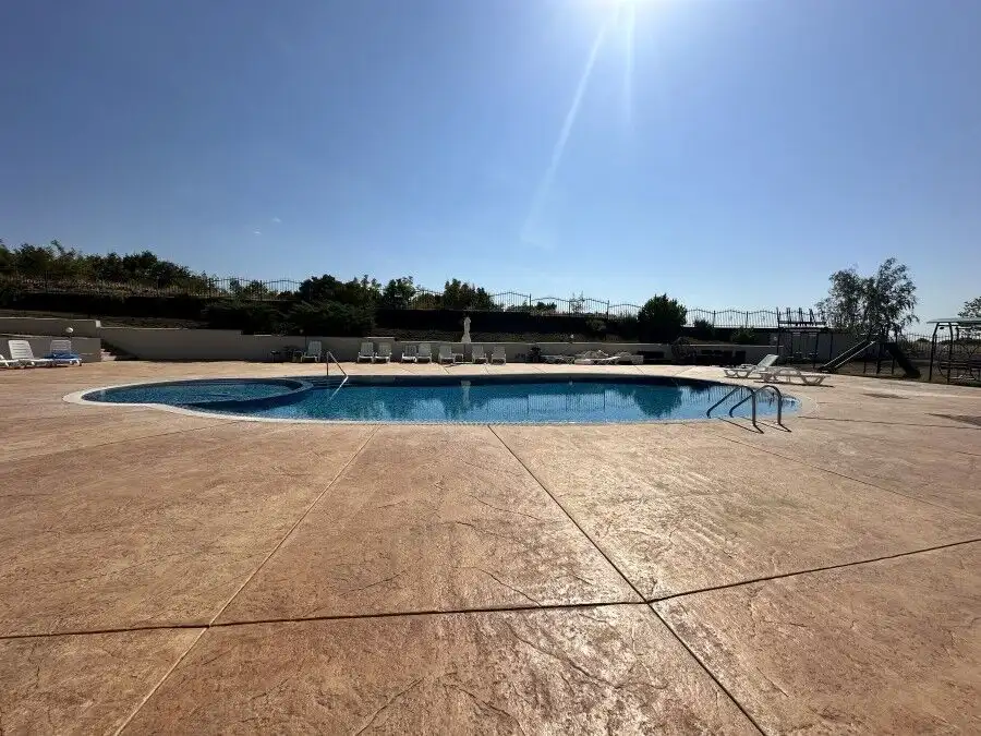 Outdoor swimming pool with sun loungers and bright sunlight.