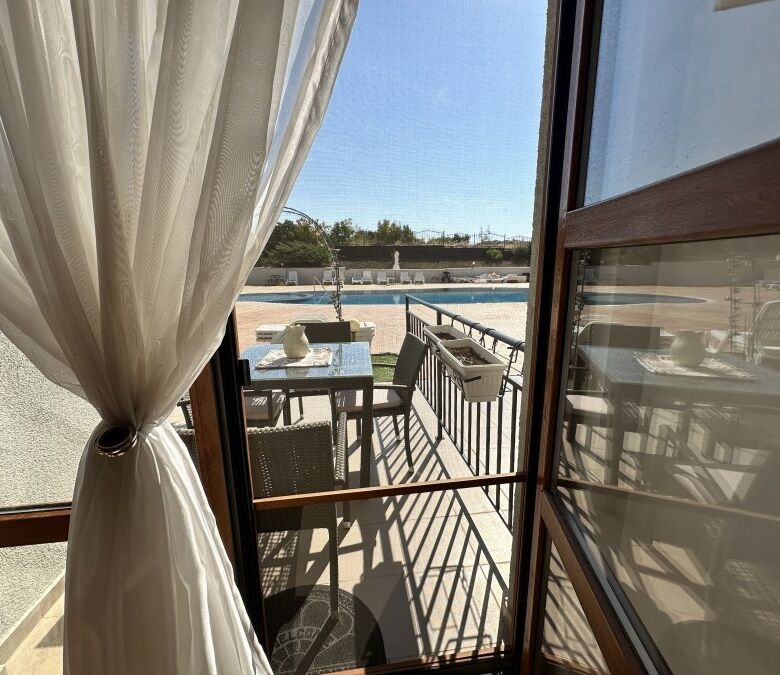 Bright apartment with balcony overlooking pool and outdoor seating area.