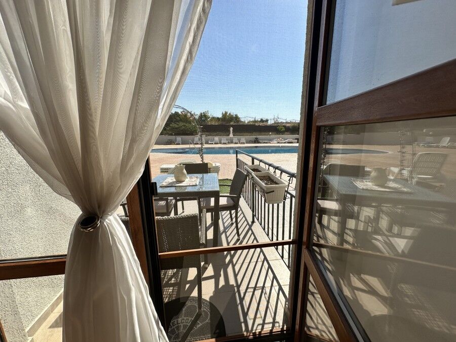 Bright apartment with balcony overlooking pool and outdoor seating area.