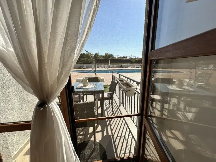 Bright apartment with balcony overlooking pool and outdoor seating area.