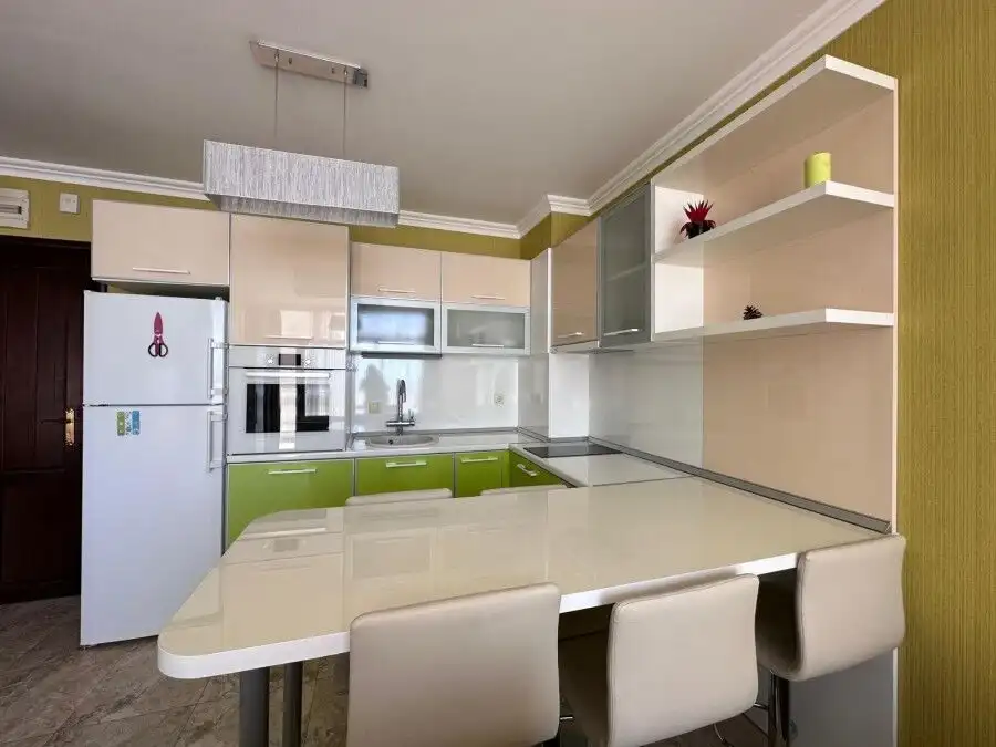 Bright, contemporary kitchen featuring green and white cabinets, a large dining table, and open shel.