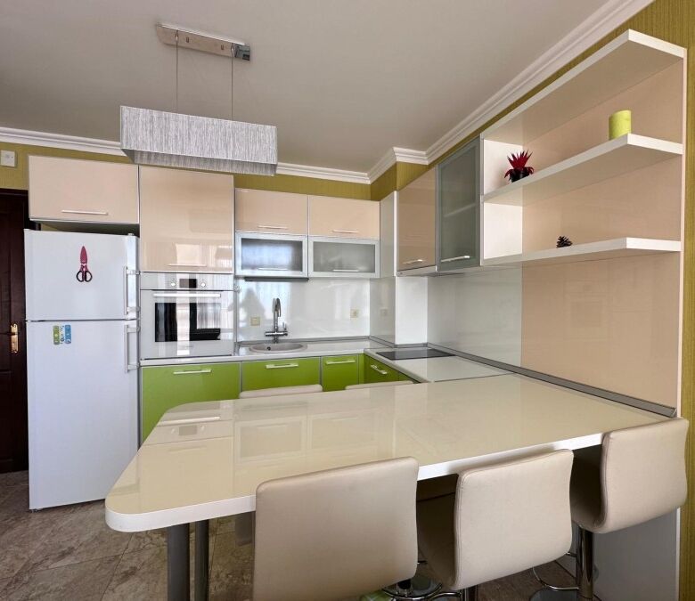 Bright, fully equipped kitchen with green accents and seating area in a seaside apartment.