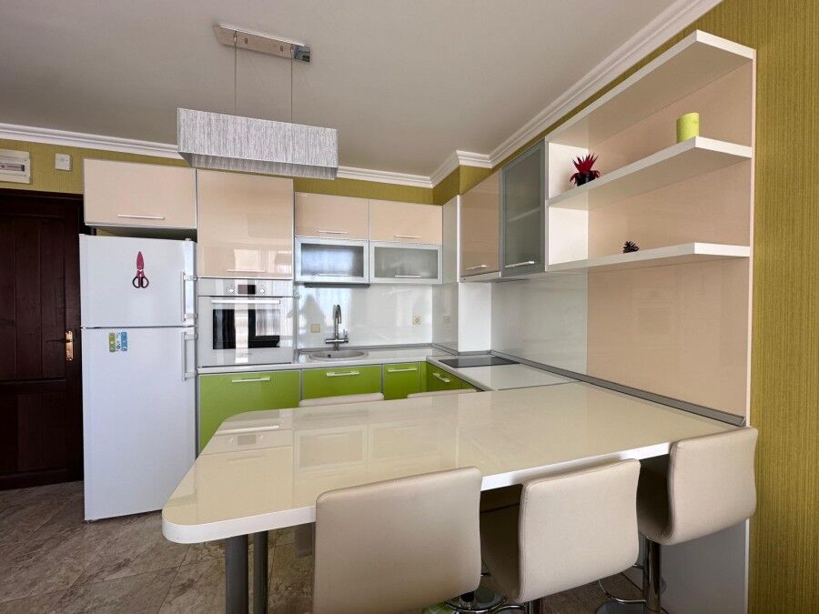 Bright, fully equipped kitchen with green accents and seating area in a seaside apartment.