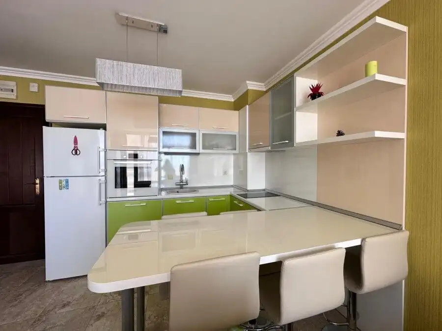Bright, fully equipped kitchen with green accents and seating area in a seaside apartment.