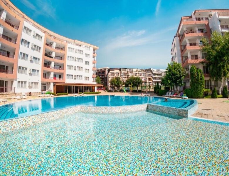 Apartment complex with swimming pool, modern buildings, and lush greenery in Ravda.