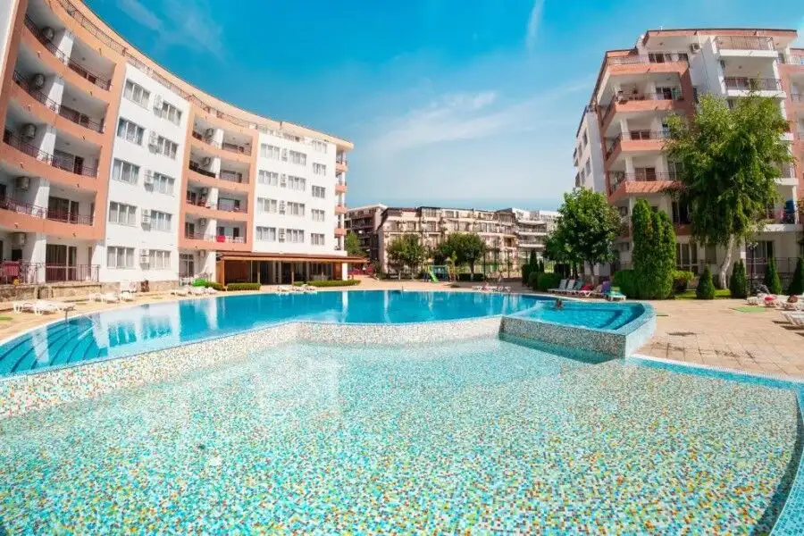 Apartment complex with swimming pool, modern buildings, and lush greenery in Ravda.