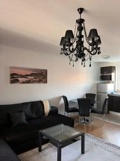 Luxurious apartment interior with black chandelier, sofa, and dining area.