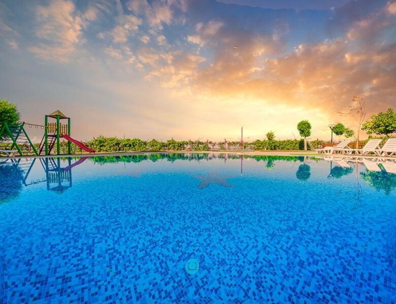 Outdoor swimming pool at Nessebar Fort Club with sunset sky and surrounding greenery.