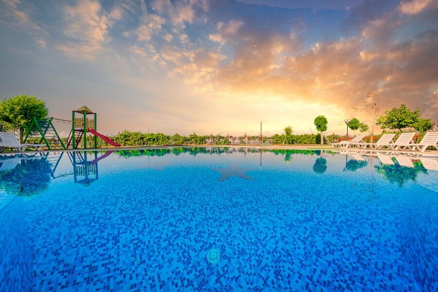 Outdoor swimming pool at Nessebar Fort Club with sunset sky and surrounding greenery.