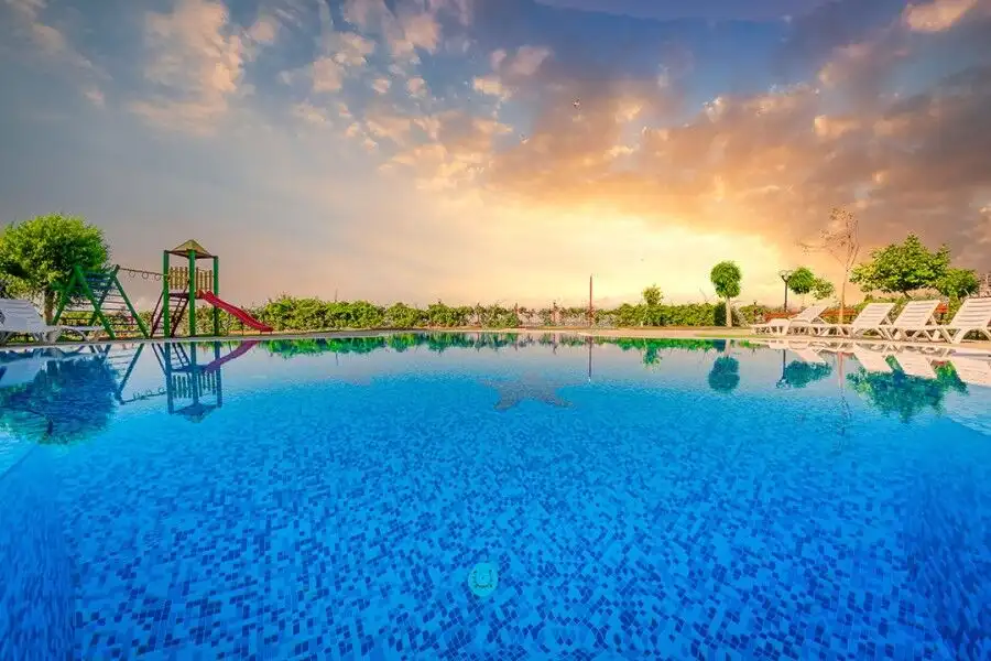 Outdoor swimming pool at Nessebar Fort Club with sunset sky and surrounding greenery.