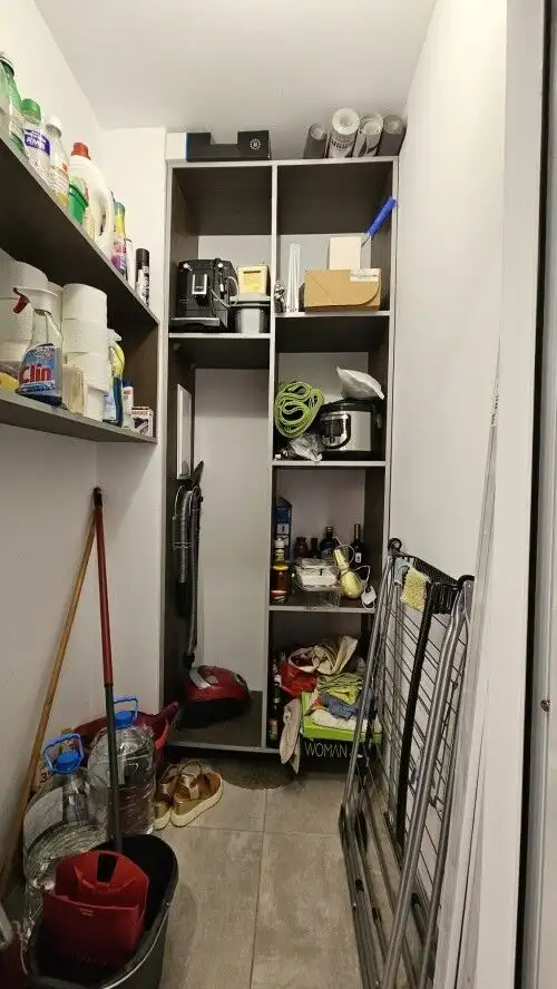 Closet with cleaning tools, bottles, and household essentials in a small utility space.