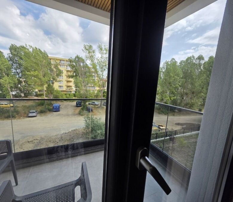 Bright view from the apartment balcony overlooking greenery and nearby buildings.