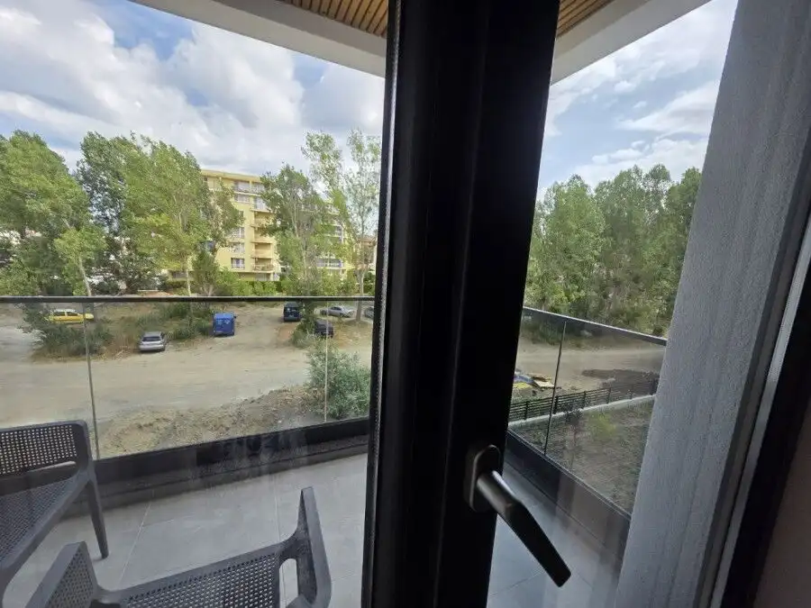 Bright view from the apartment balcony overlooking greenery and nearby buildings.