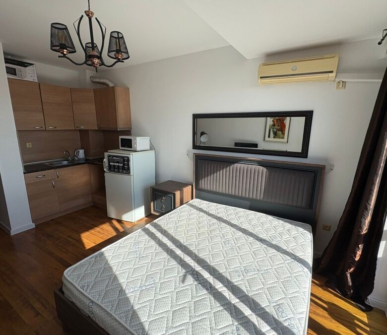 Studio apartment with modern interior, large window, and balcony overlooking the sea and pool.