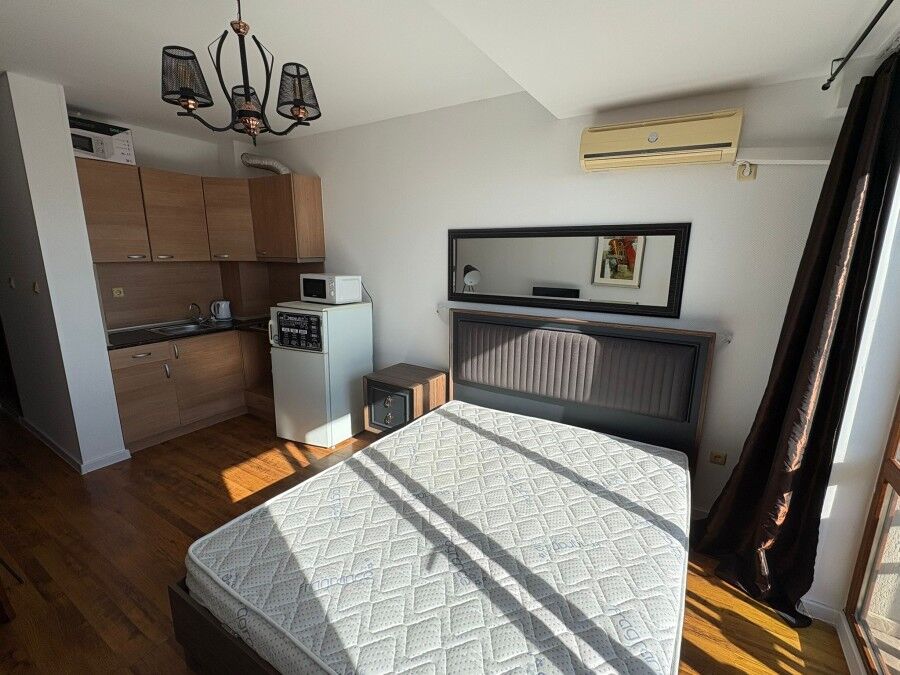 Studio apartment with modern interior, large window, and balcony overlooking the sea and pool.