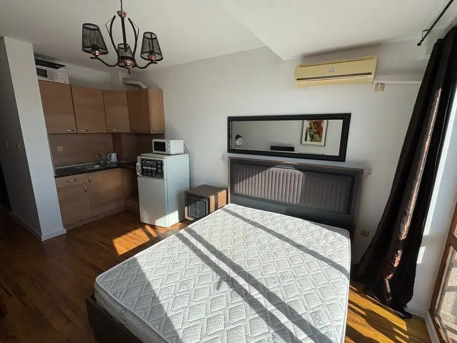 Studio apartment with modern interior, large window, and balcony overlooking the sea and pool.