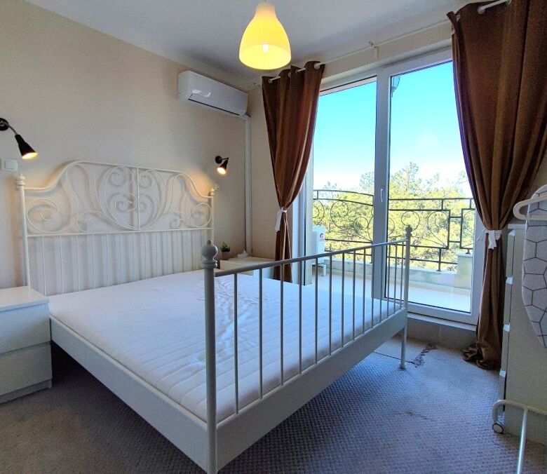 Cozy bedroom with large window, balcony access, and scenic views in Pomorie Residence.