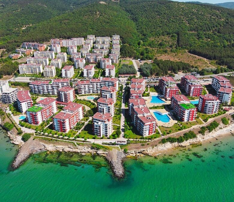 Aerial view of a coastal apartment community with colorful buildings, pools, and scenic sea views.