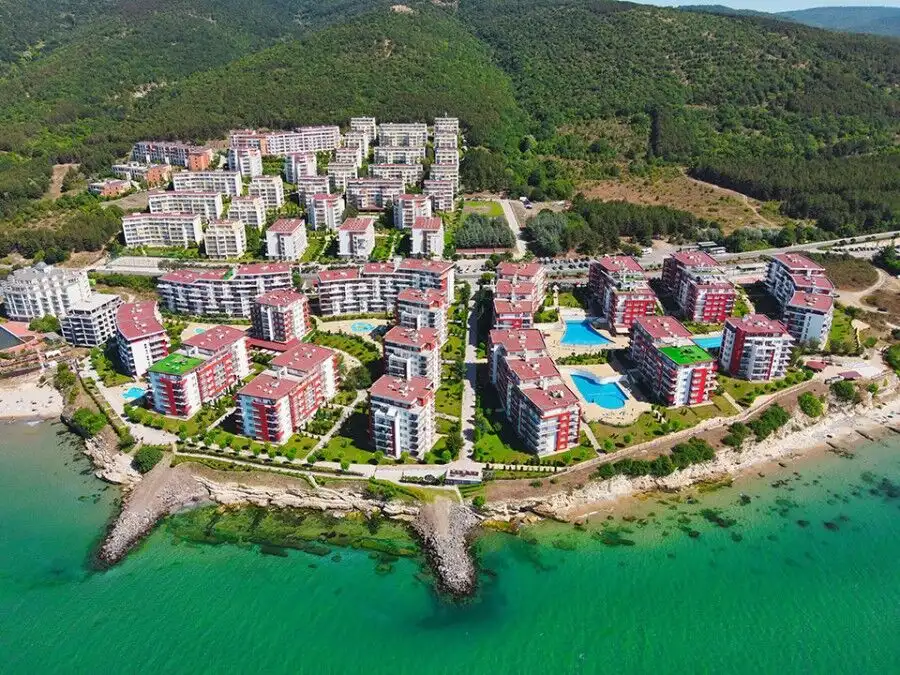 Aerial view of a coastal apartment community with colorful buildings, pools, and scenic sea views.