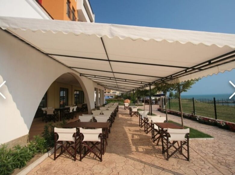 Seaside outdoor dining with tables and chairs under a large canopy at Marina Cape, Aheloy.