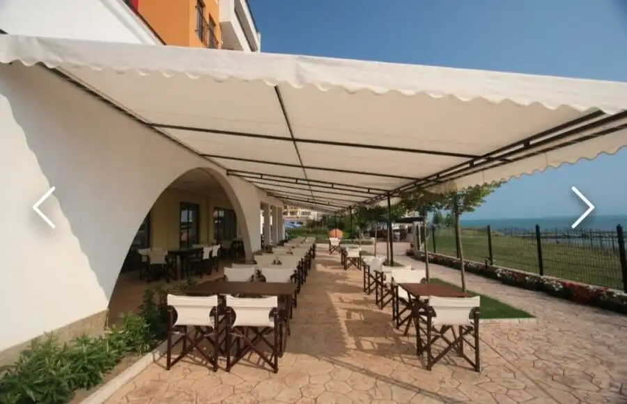 Seaside outdoor dining with tables and chairs under a large canopy at Marina Cape, Aheloy.