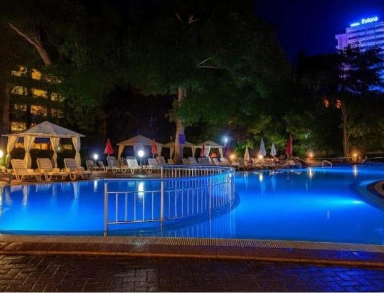 Night view of illuminated swimming pool with lounge chairs and umbrellas.