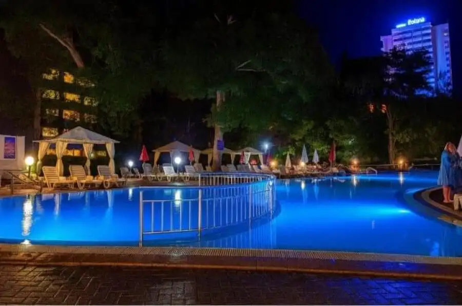Night view of illuminated swimming pool with lounge chairs and umbrellas.