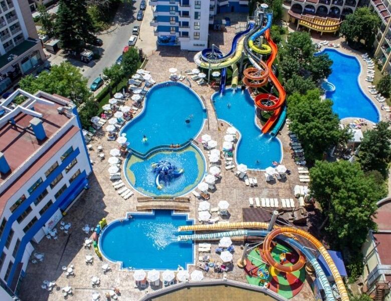 Pool with water slides and sun loungers in a sunny apartment complex.