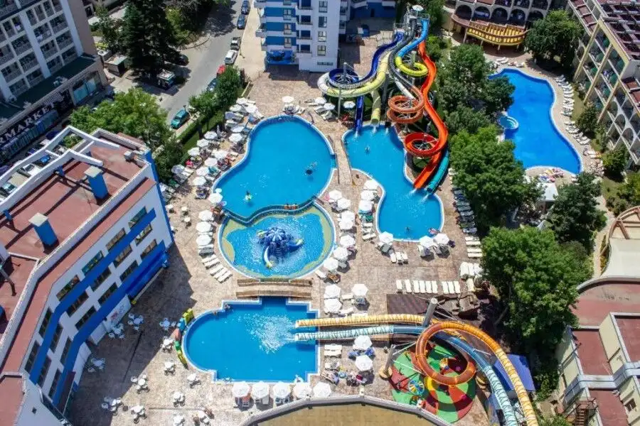 Pool with water slides and sun loungers in a sunny apartment complex.
