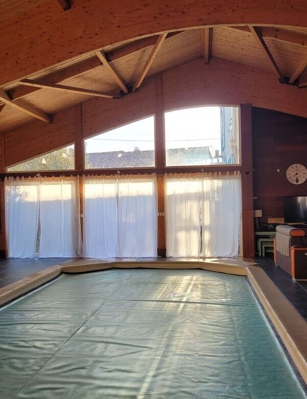 Indoor swimming pool with wooden ceiling and large windows in Aumagne property.