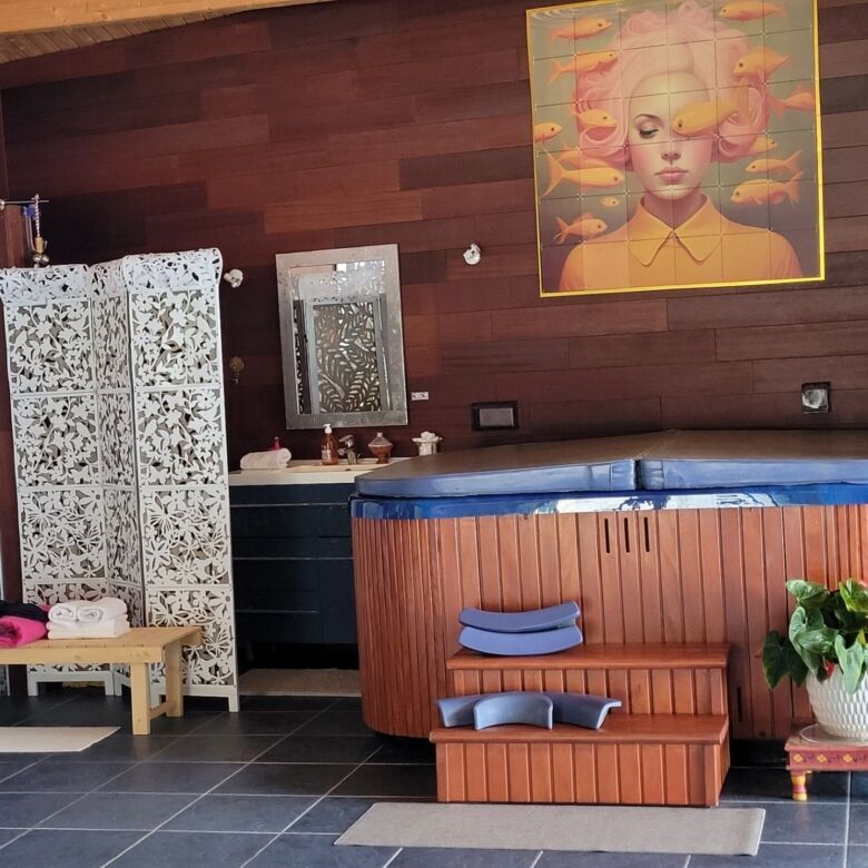 Relaxing indoor spa with a wooden hot tub, vibrant artwork, and elegant privacy screens for a luxuri.