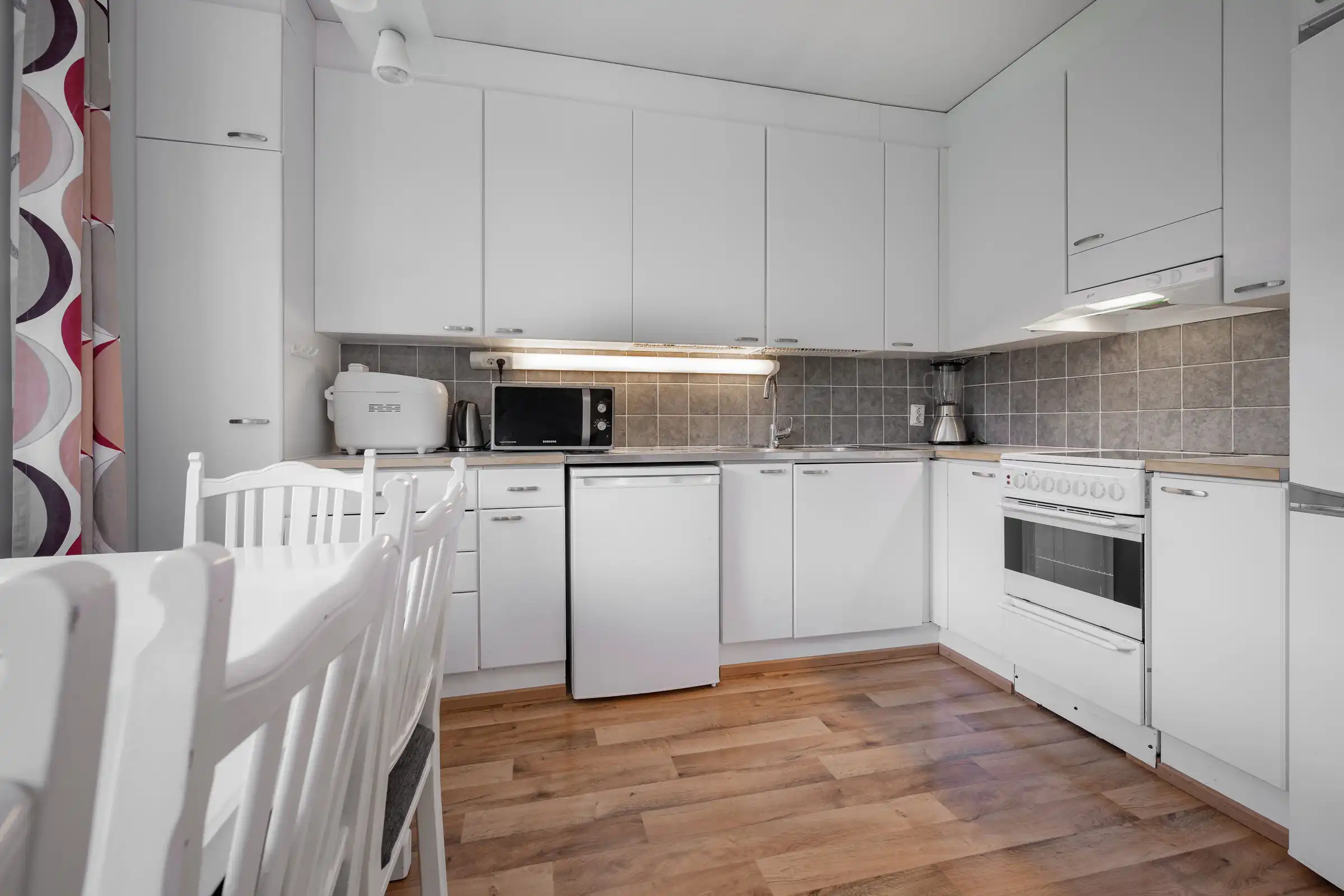 Bright, clean kitchen with white cabinets, appliances, and a dining table in a serene home setting.