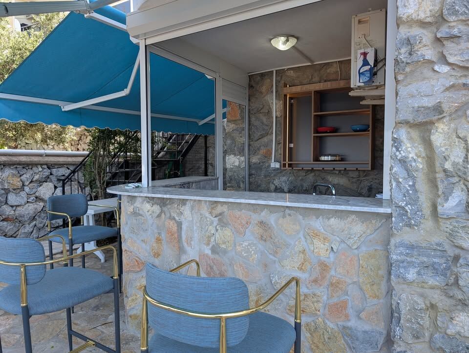 Outdoor bar with stone facade, seating, and blue awning for relaxing gatherings.