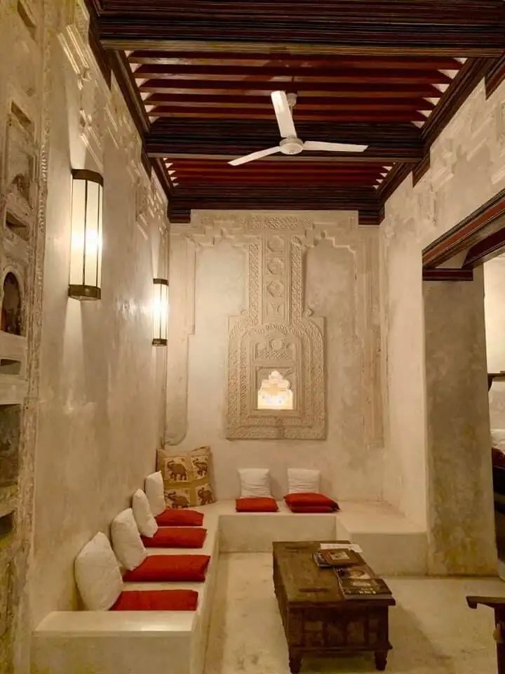 Lamu house interior with carved walls, cushions, and wooden furniture.