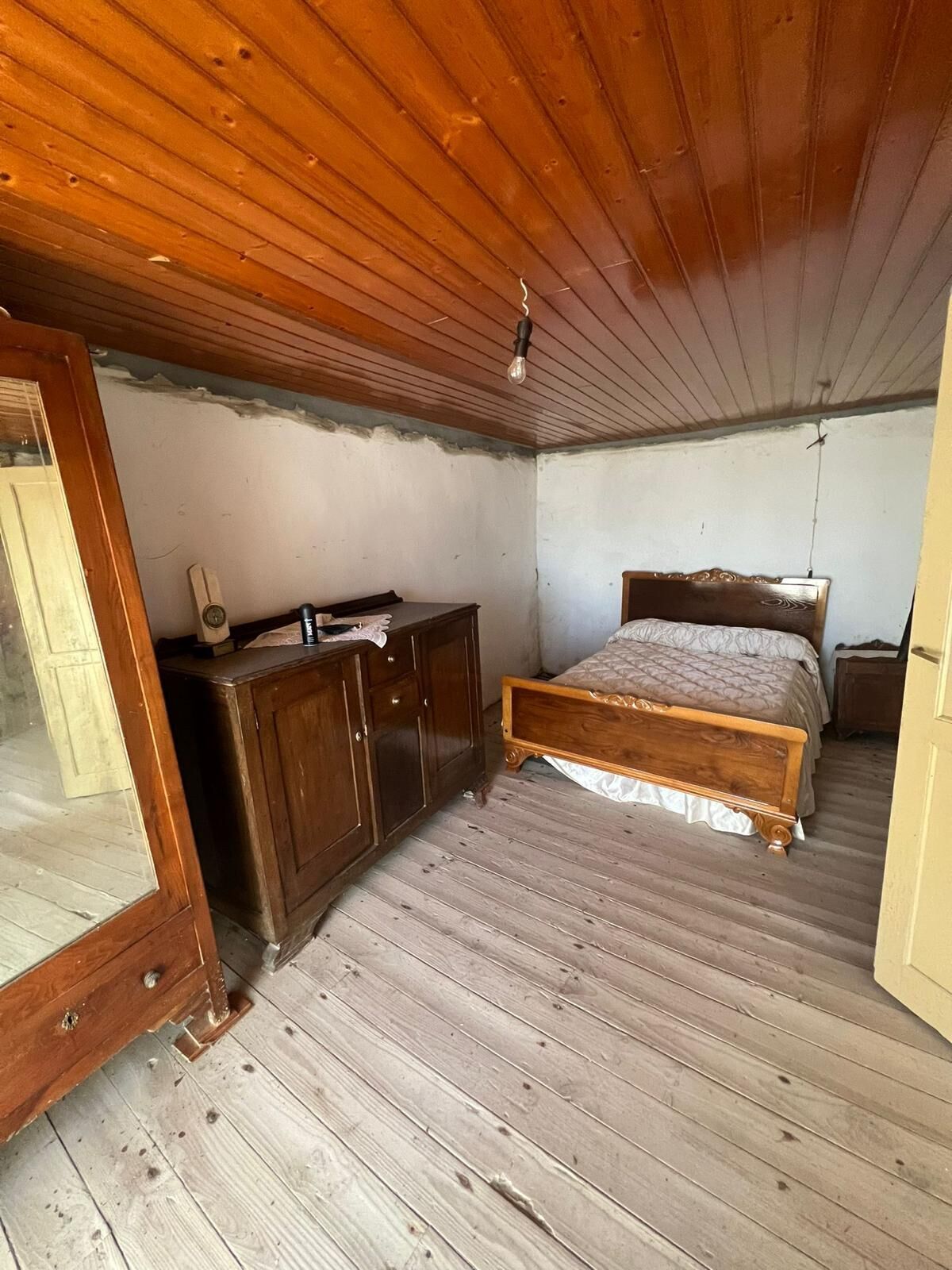 Comfortable bedroom with wooden ceiling and flooring, featuring a bed and vintage furniture.