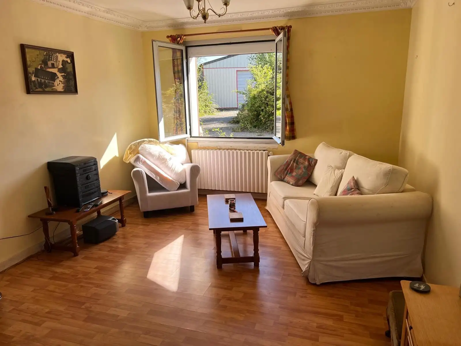 Bright living room with large open window overlooking garden in Vautorte. Comfortable sofas and wood.