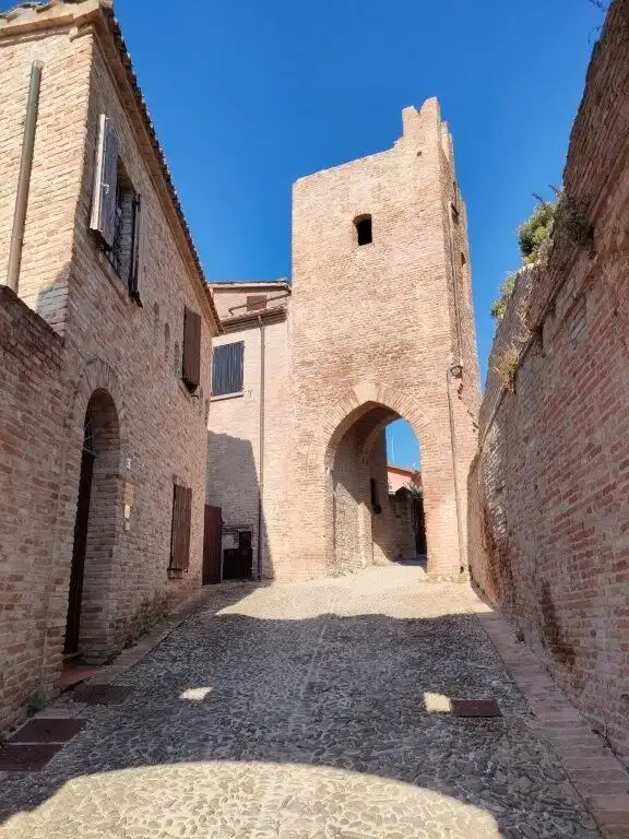 Historic castle gate in Coriano Rimini, Italy, with brick walls and cobblestone street under a clear.