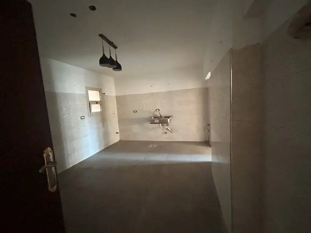 Spacious empty kitchen with tiled walls and ceiling lighting.