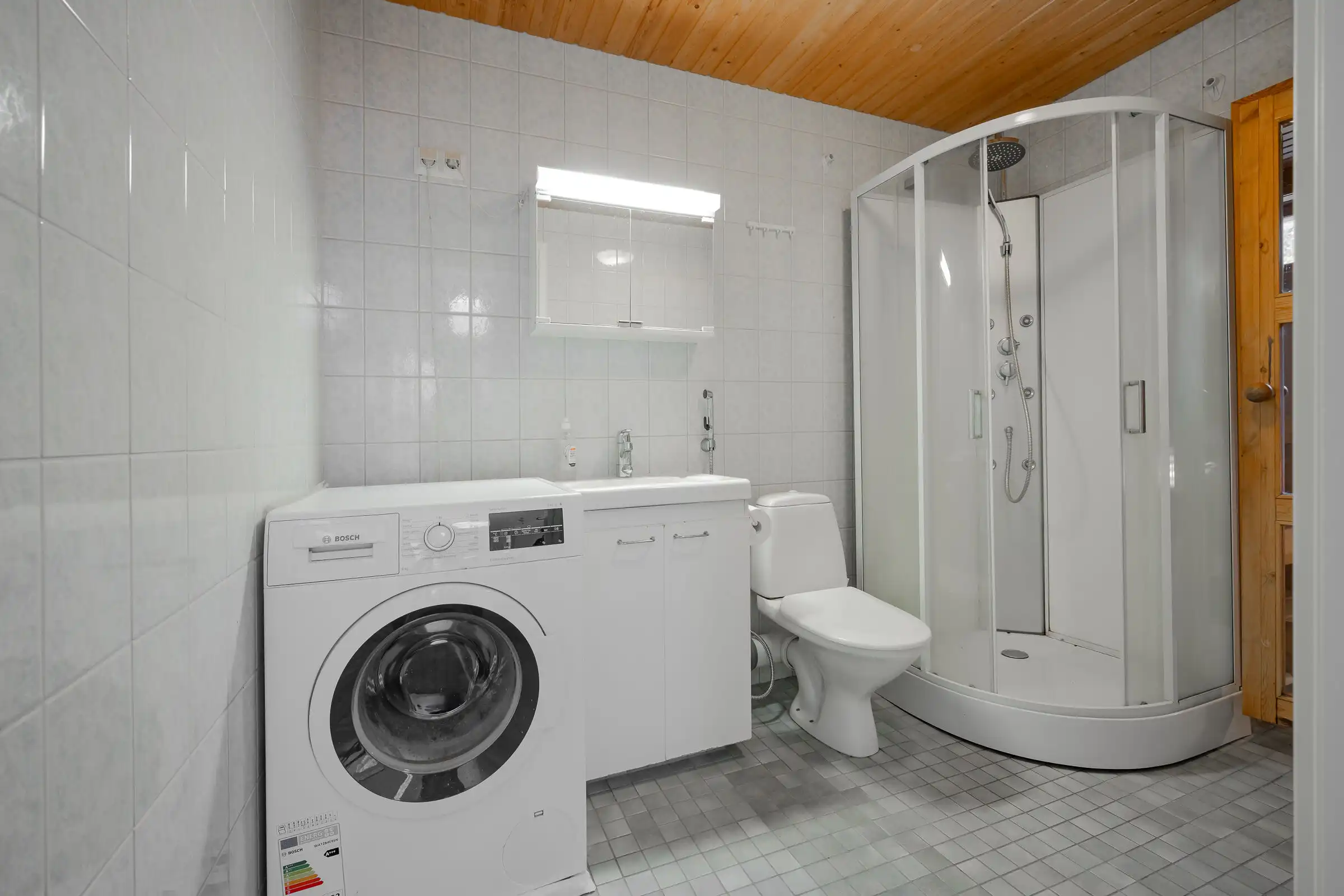 Modern bathroom with washing machine and shower cabin in a serene Finnish home.