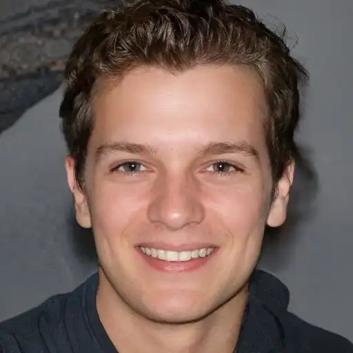 Young man with a friendly smile, wearing a dark shirt, in a close-up portrait.
