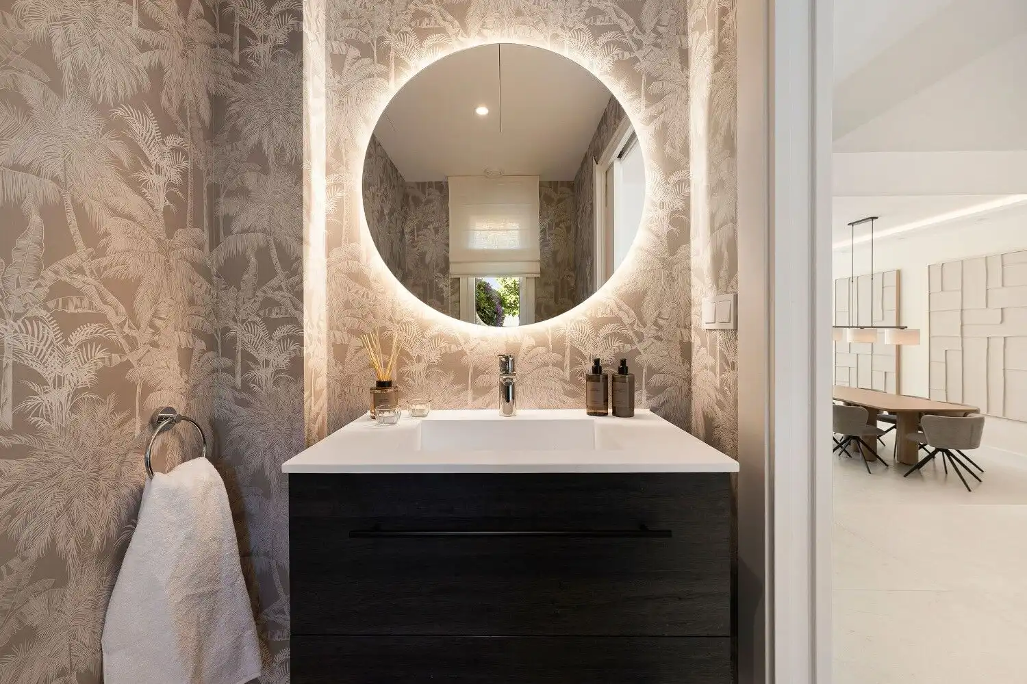 Modern bathroom vanity with a round illuminated mirror and stylish wallpaper.