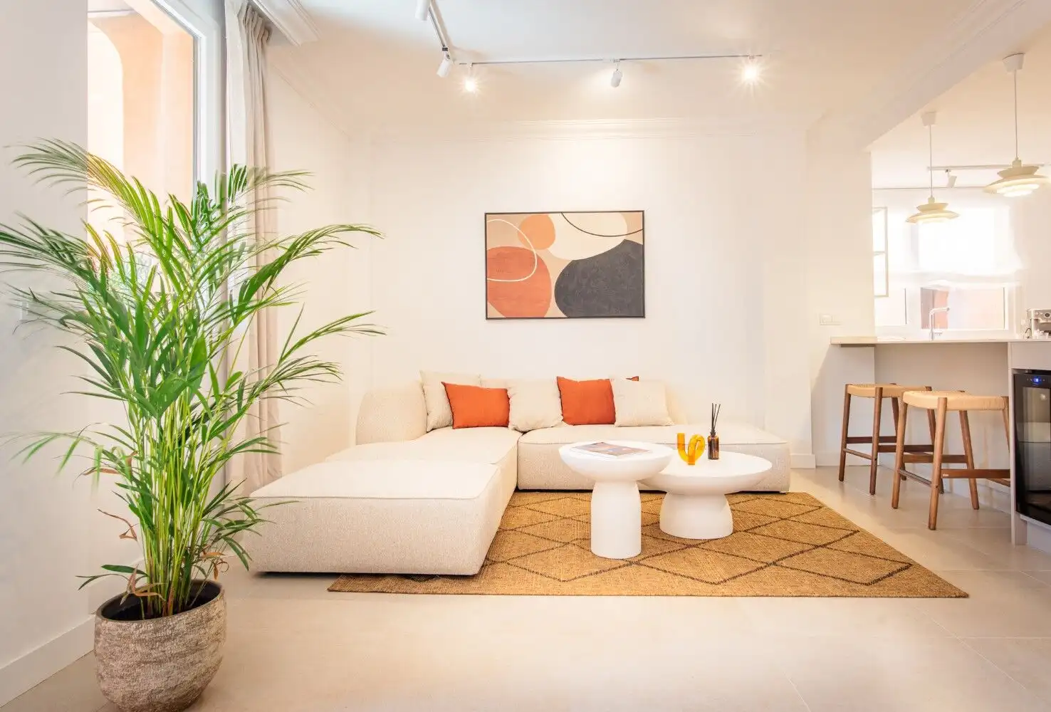 Modern living room featuring a white sofa with orange cushions, a potted plant, and contemporary wal.