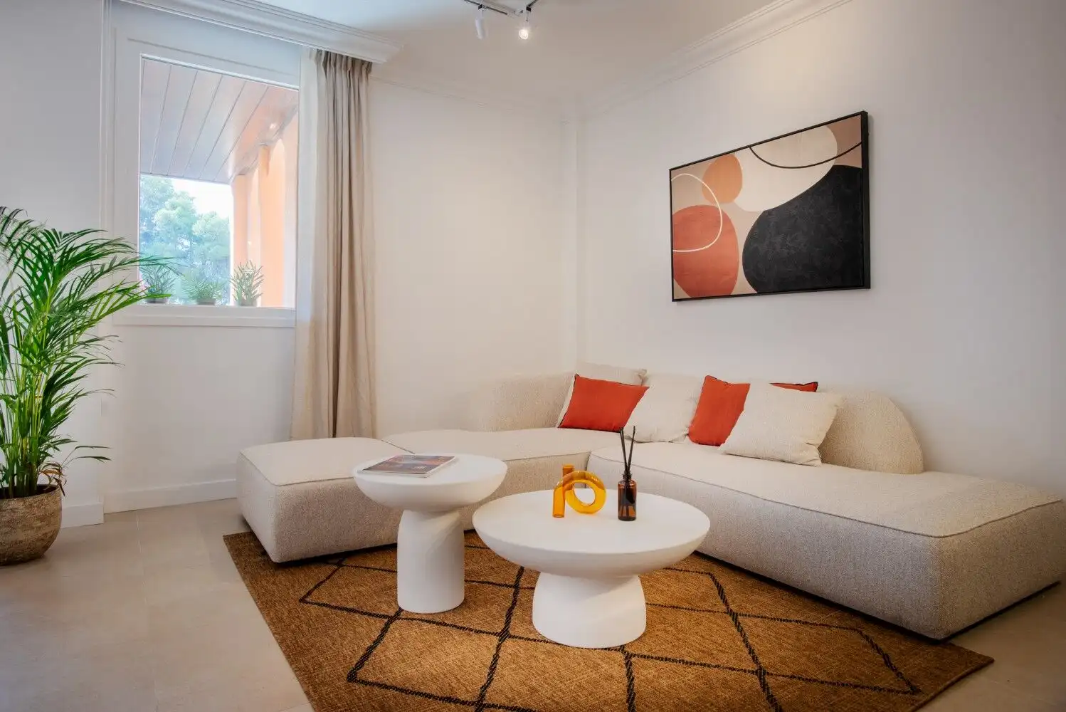 Bright living room with modern decor, white sofa, colorful cushions, and stylish coffee tables.