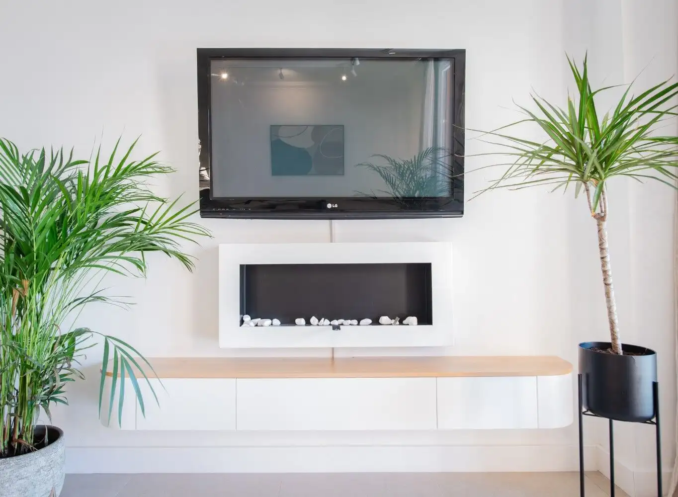 Contemporary living room featuring a wall-mounted TV and a sleek fireplace, with potted plants for a.